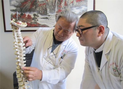 第六代传承人李寿亭（左）向其子李相伟讲解人体脊柱构造及腧穴区位